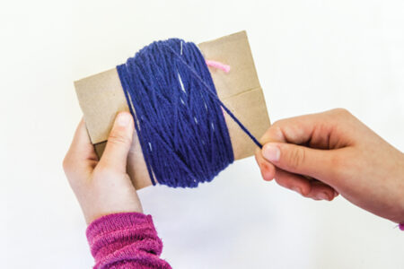 person wrapping blue yarn around cardboard